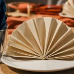Pliage en serviette en papier facile : serviette beige éventail sur table de fête